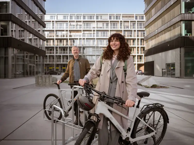 JobRadlerin steht mit Fahrrad abfahrbereit auf einem Firmencampus, im Hintergrund Kollege mit Fahrrad